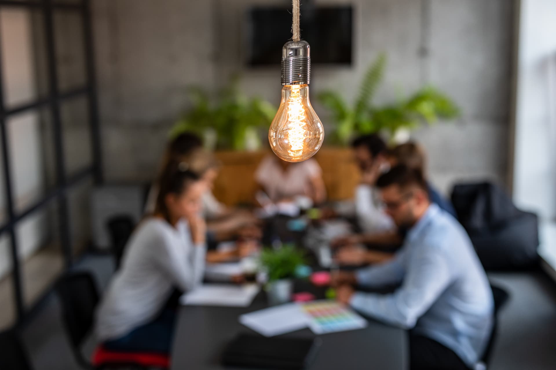 Glödlampa i förgrunden framför kollegor som håller möte om ekonomi på ett modernt kontor
